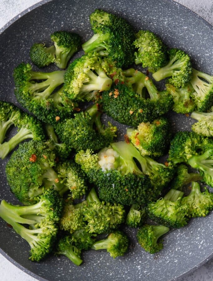 A bunch of broccoli florets sautéing in a pan.