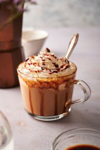 Whipped cream with caramel sauce on it on top of a caramel macchiato.