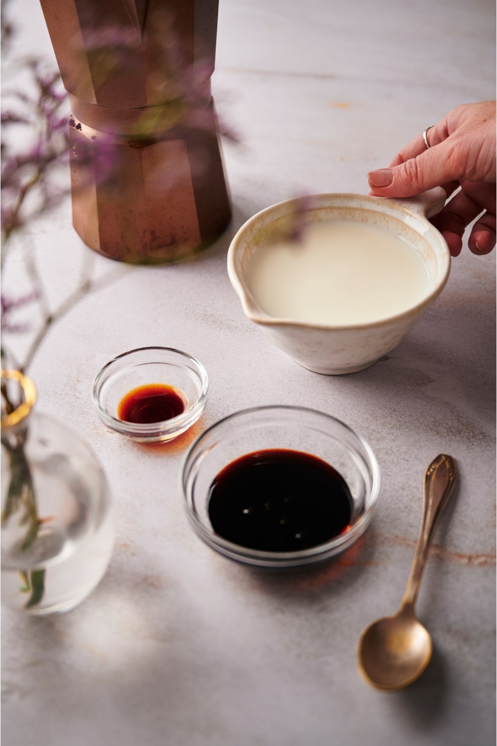 A bowl of almond milk, a bowl of espresso, and a bowl of vanilla extract on a grey counter.