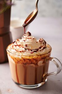 A spoon drizzling caramel sauce on top of whipped cream in a glass.