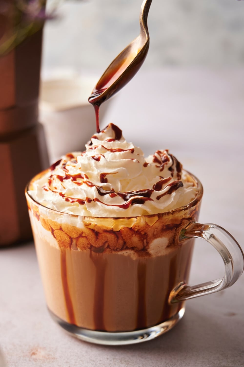 A spoon drizzling caramel sauce on top of whipped cream in a glass.