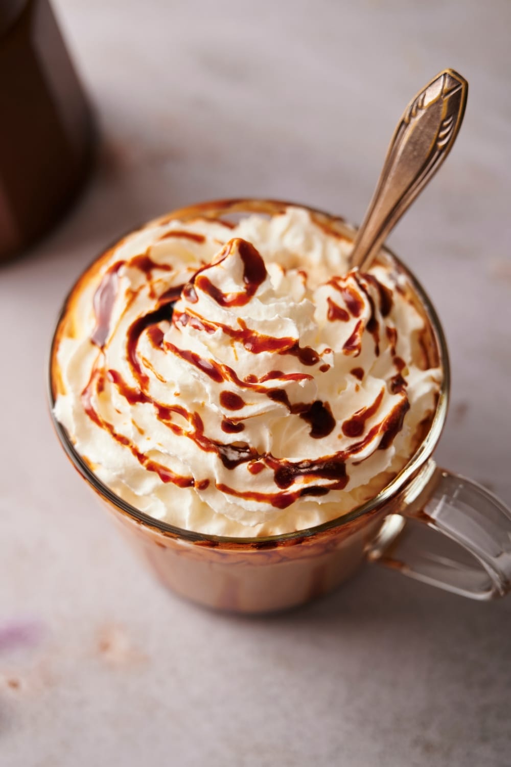 A spoon in a glass that has caramel sauce on top of whipped cream.