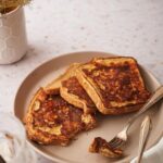 Three french toast slices arranged on a plate with a fork holding a piece of one of the french toasts.