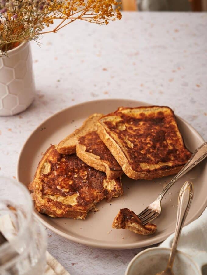 Three french toast slices arranged on a plate with a fork holding a piece of one of the french toasts.