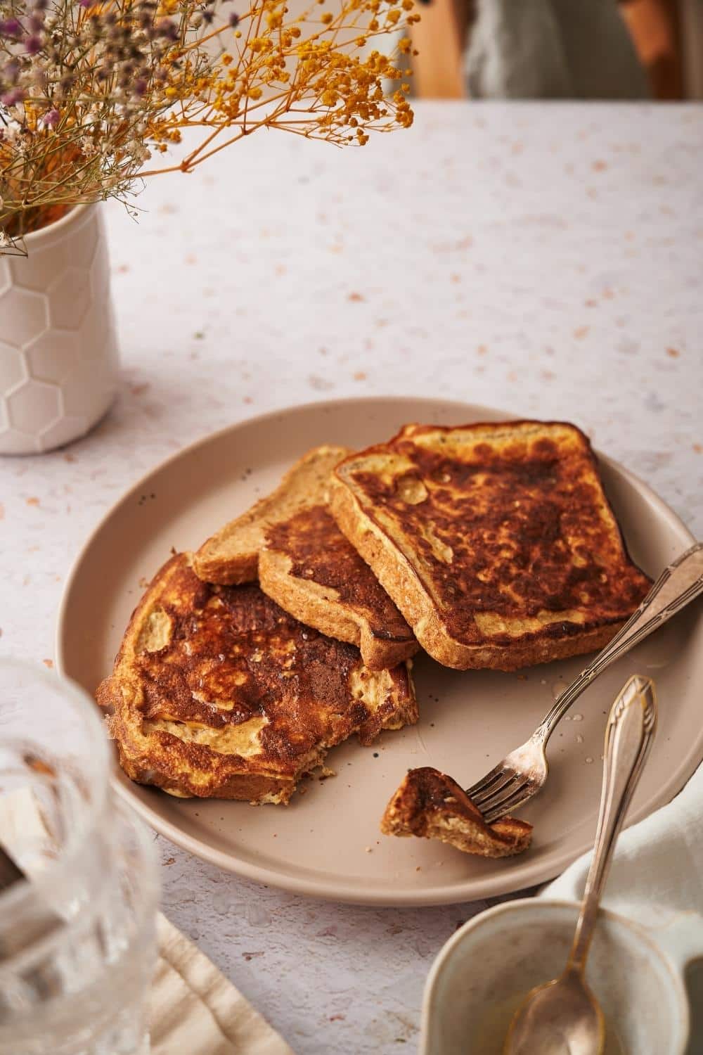 Three french toast slices arranged on a plate with a fork holding a piece of one of the french toasts.