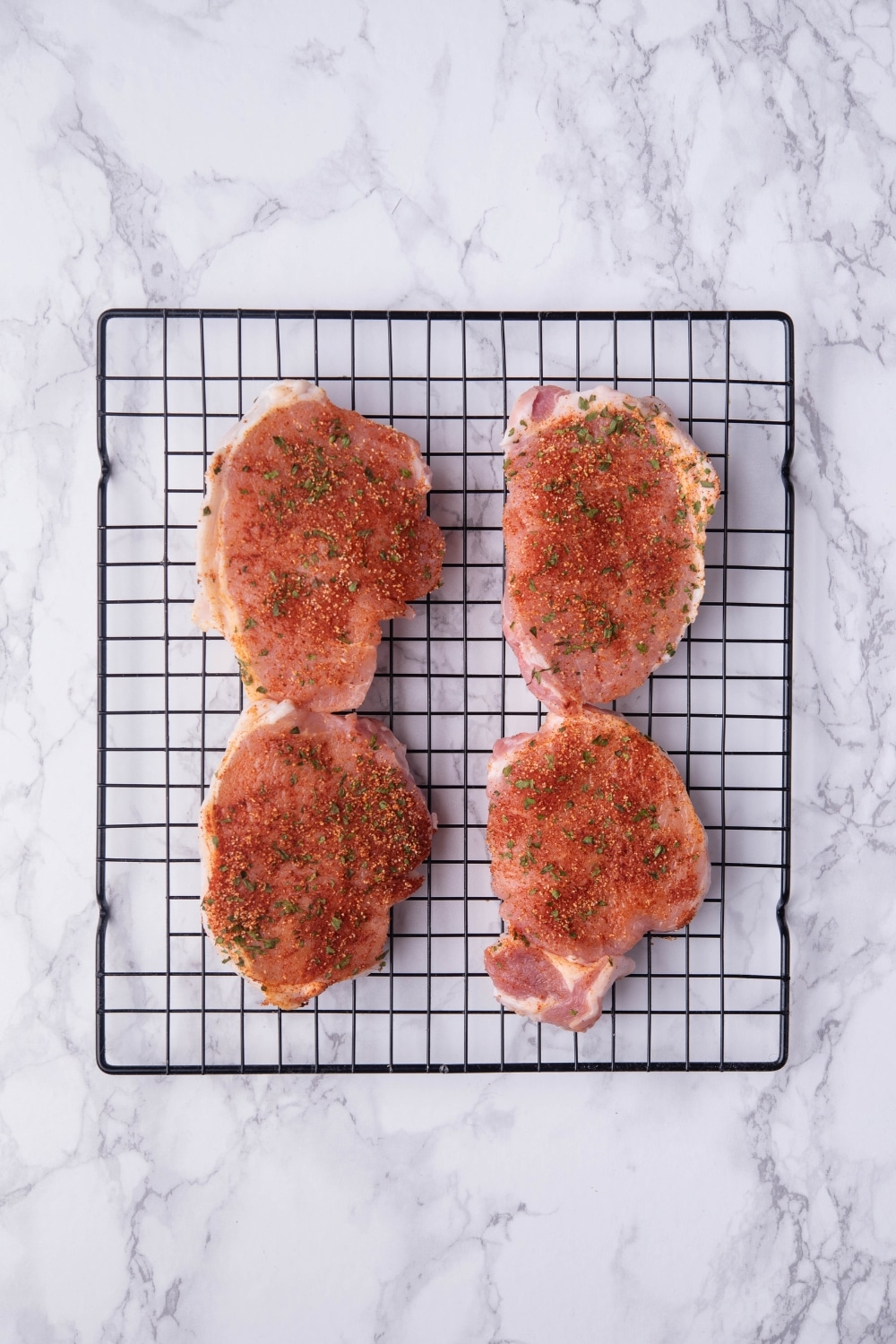 Four seasoned pork chops on a black drying rack.