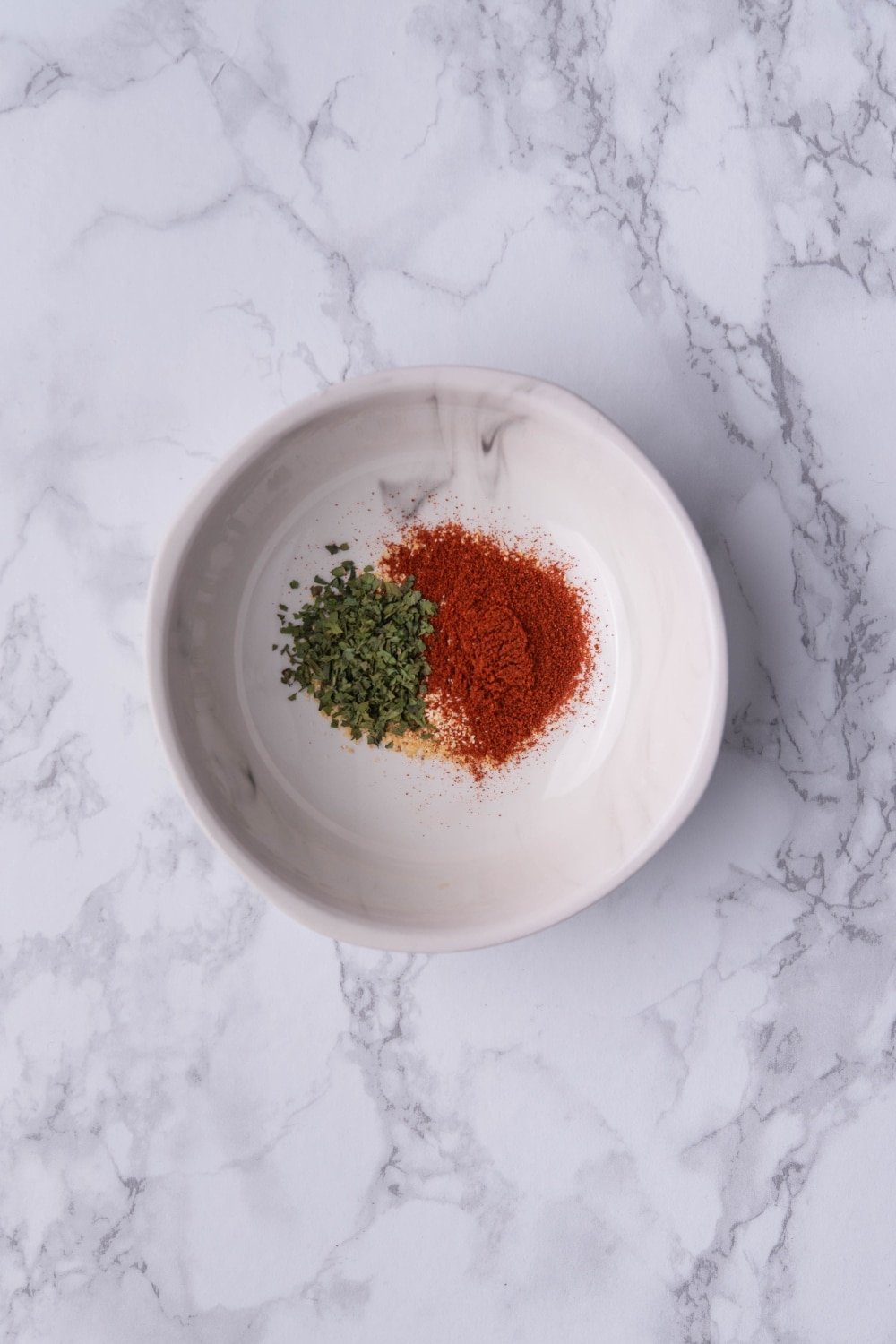 A small white plate of paprika, garlic powder, onion powder, and dried parsley.