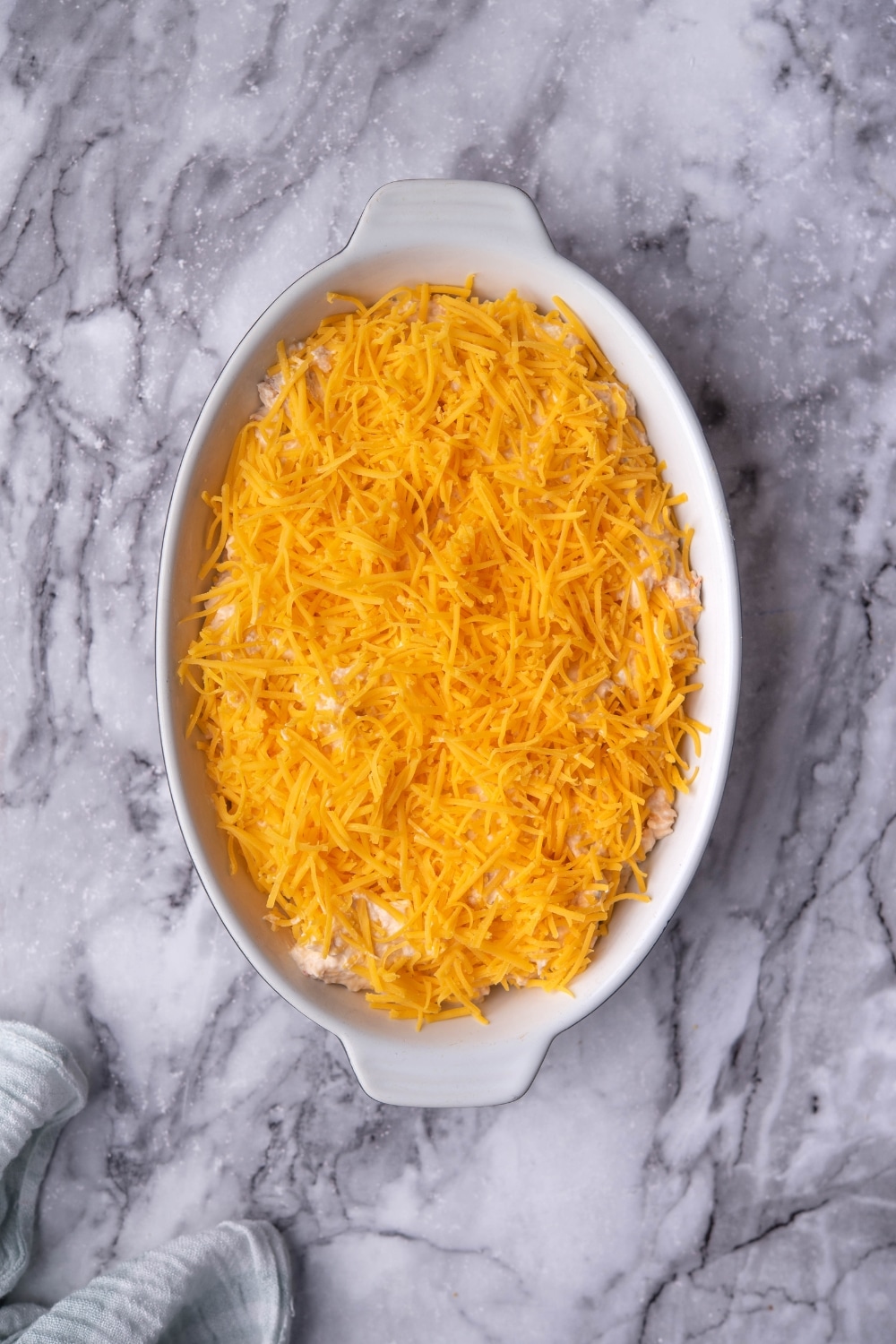 A baking dish of healthy chicken dip topped with a layer of shredded cheddar cheese.