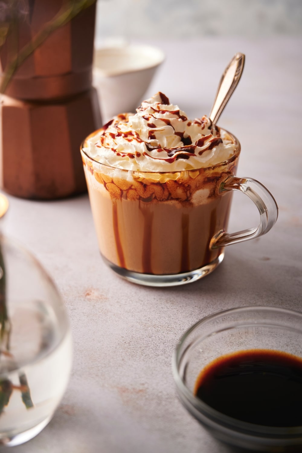 Part of a bowl of caramel sauce with a glass this filled with caramel macchiato with whipped cream and caramel sauce on top.