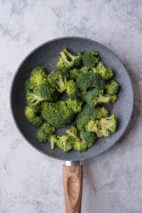 Uncooked broccoli florets on a grey speckled skillet with a wooden handle.