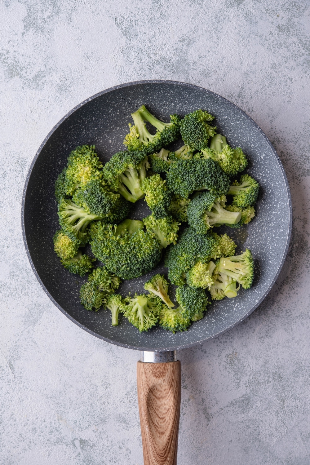 Uncooked broccoli florets on a grey speckled skillet with a wooden handle.