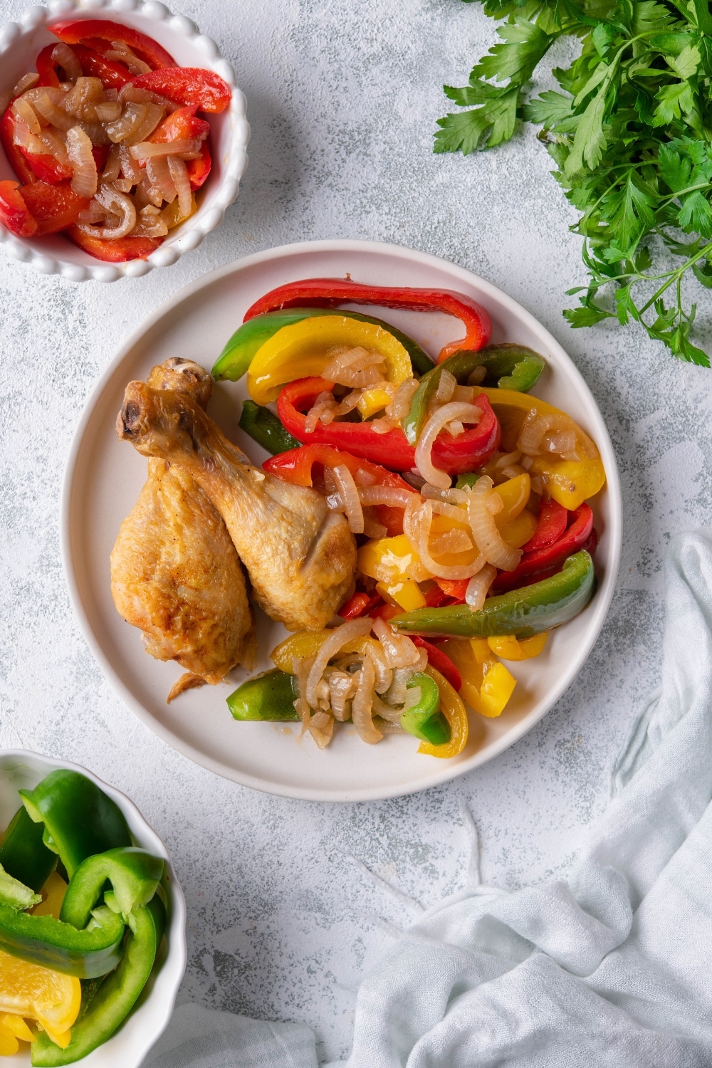 Top view of sauteed bell peppers and onions served with fried chicken on a white plate. Next to it is a small bowl with more sauteed bell peppers and onions and a bowl of uncooked sliced peppers.