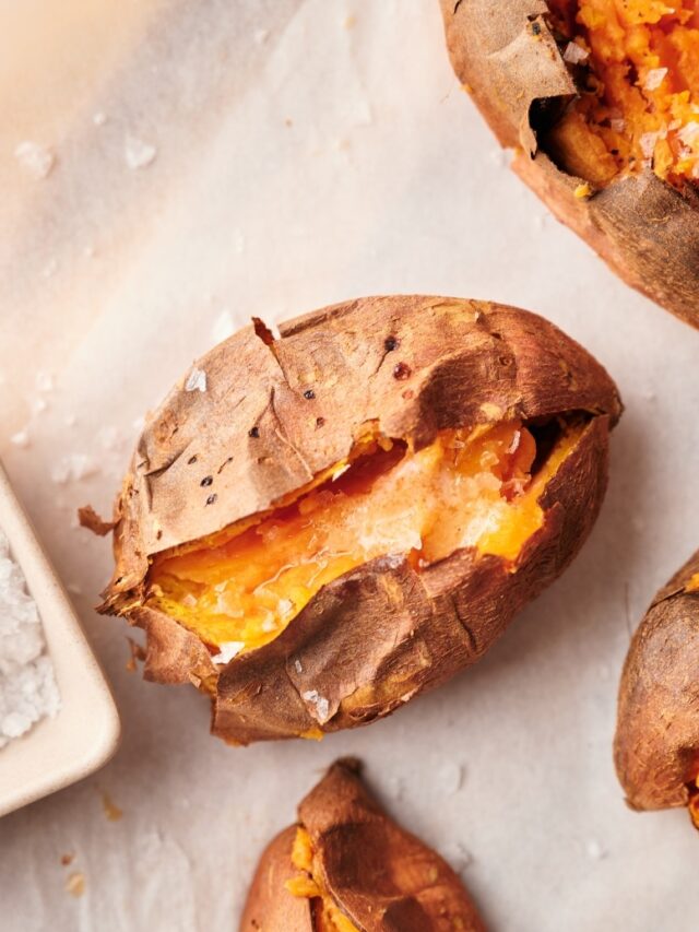 Close up of baked sweet potatoes cut open and arranged on a parchment paper lined wooden cutting board. Part of a square dipping bowl filled with salt is on the side.