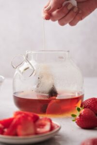 A hand dipping two tea bags into a pot of water.