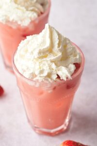 Whipped cream on top of a creamy pink drink in a glass.