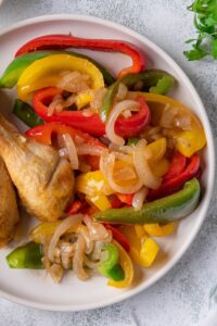 Top view of sauteed bell peppers and onions garnished with fresh parsley on a white plate. Part of 2 pieces of fried chicken can be seen on the side on the same plate.