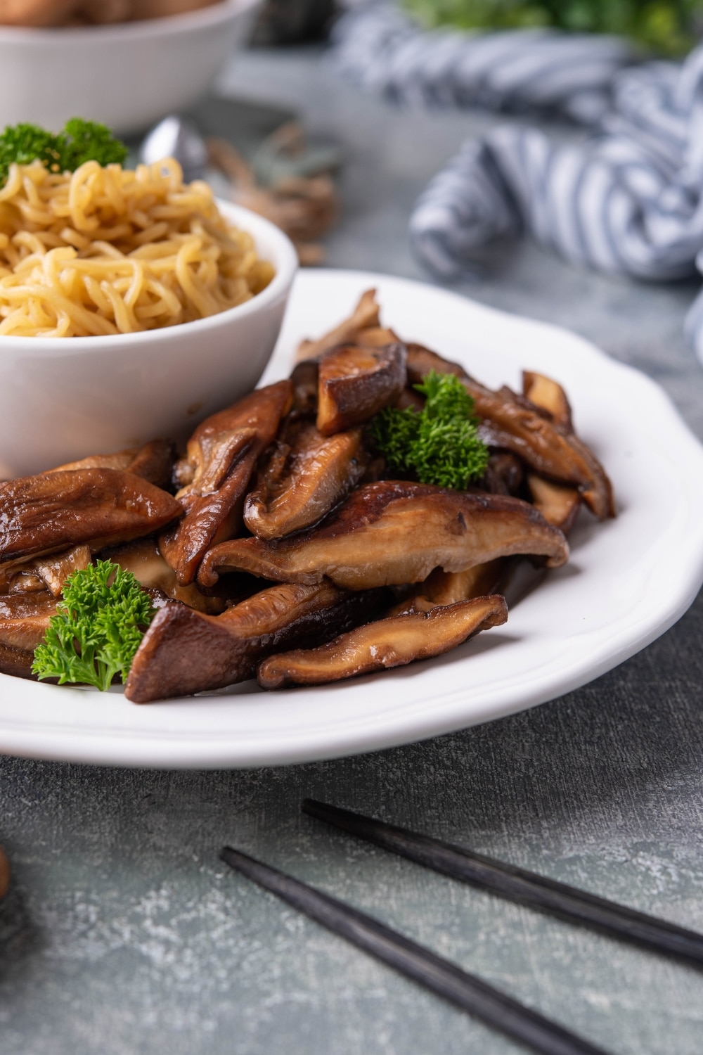 A plate of sauteed shiitake mushrooms garnished with parsley. A small bowl of noodles is also on the plate.