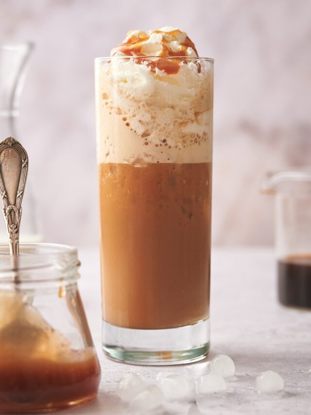 Whipped cream with caramel sauce on it in a glass that is filled with a keto frappuccino.