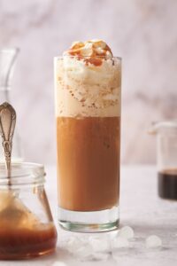 Whipped cream with caramel sauce on it in a glass that is filled with a keto frappuccino.