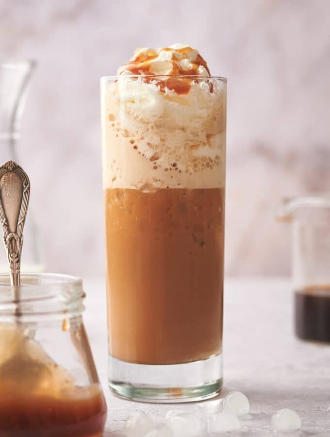 Whipped cream with caramel sauce on it in a glass that is filled with a keto frappuccino.