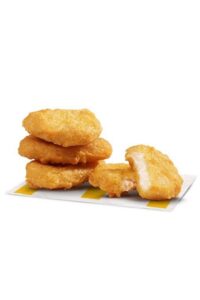 Three chicken nuggets stacked on top of one another with a chicken nugget broken in half next to the stack.