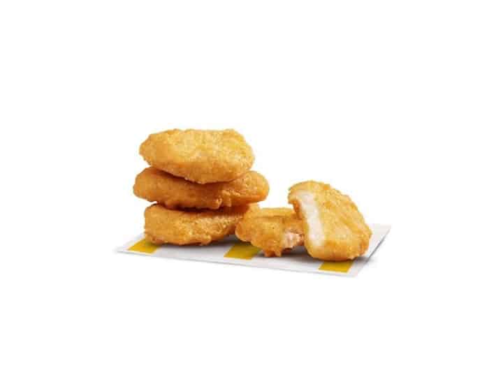 Three chicken nuggets stacked on top of one another with a chicken nugget broken in half next to the stack.