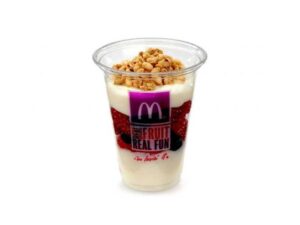 A clear cup filled with granola on top of a layer of yogurt, fruit, and another layer of yogurt.