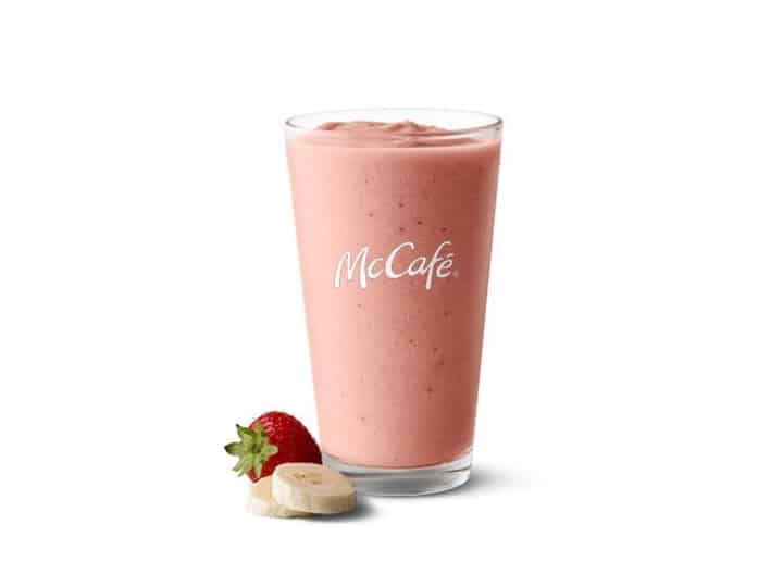 A glass cup with a strawberry banana smoothie in it.
