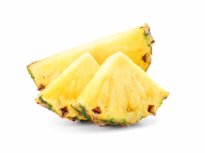 Two slices of pineapple in front of half of a pineapple.