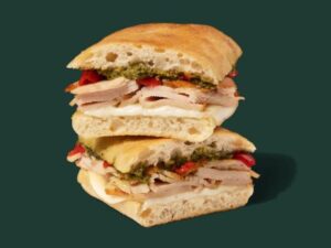 A Starbucks turkey, provolone, and pesto sandwich on a cibatta roll. The sandwich is cut in half and stacked on top of one another.