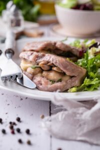 Seared pork chops stuffed with swiss cheese and mushrooms on a white plate with garden salad.