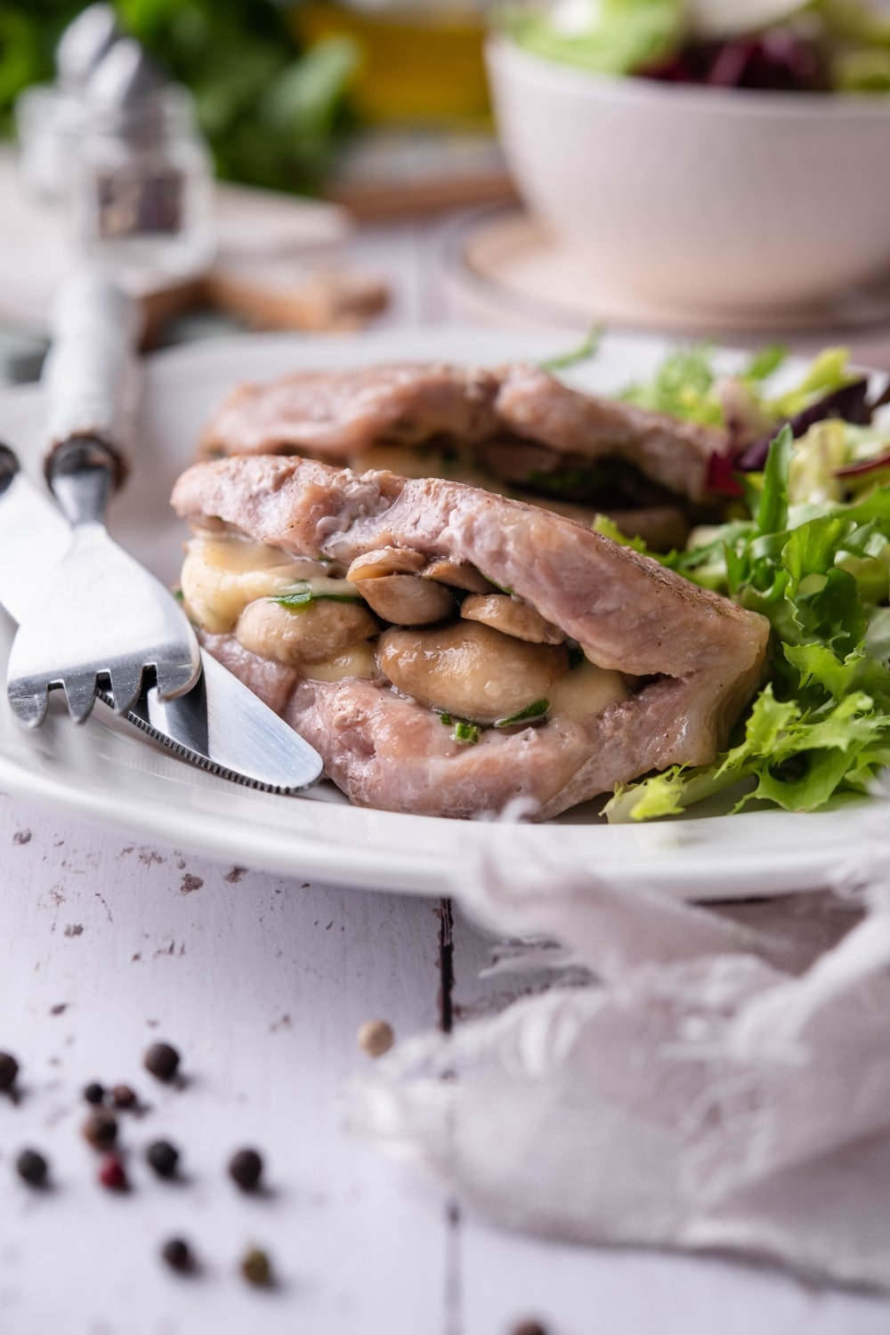 Seared pork chops stuffed with swiss cheese and mushrooms on a white plate with garden salad.