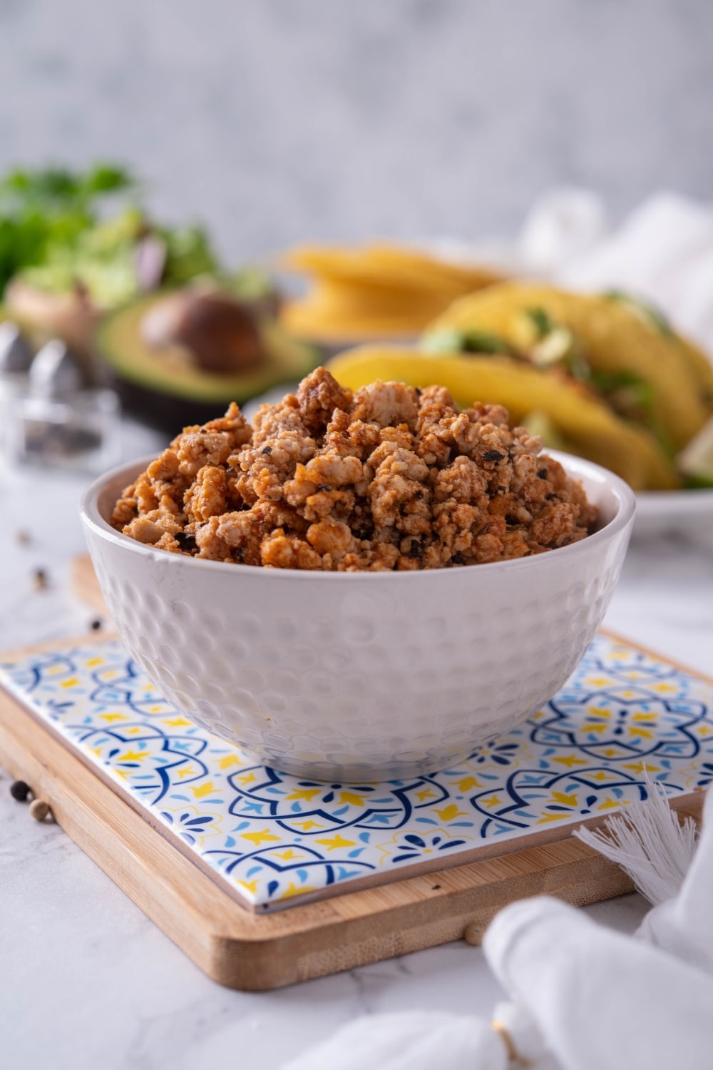 A white bowl filled with ground turkey taco meat. Behind is a plate of turkey tacos.