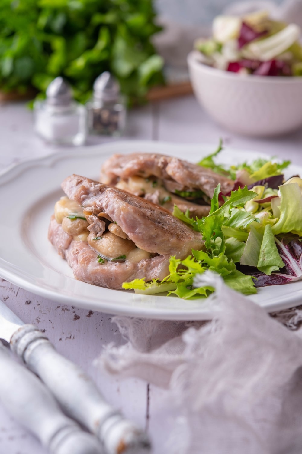 Seared pork chops stuffed with swiss cheese and mushrooms with garden salad on a white plate.