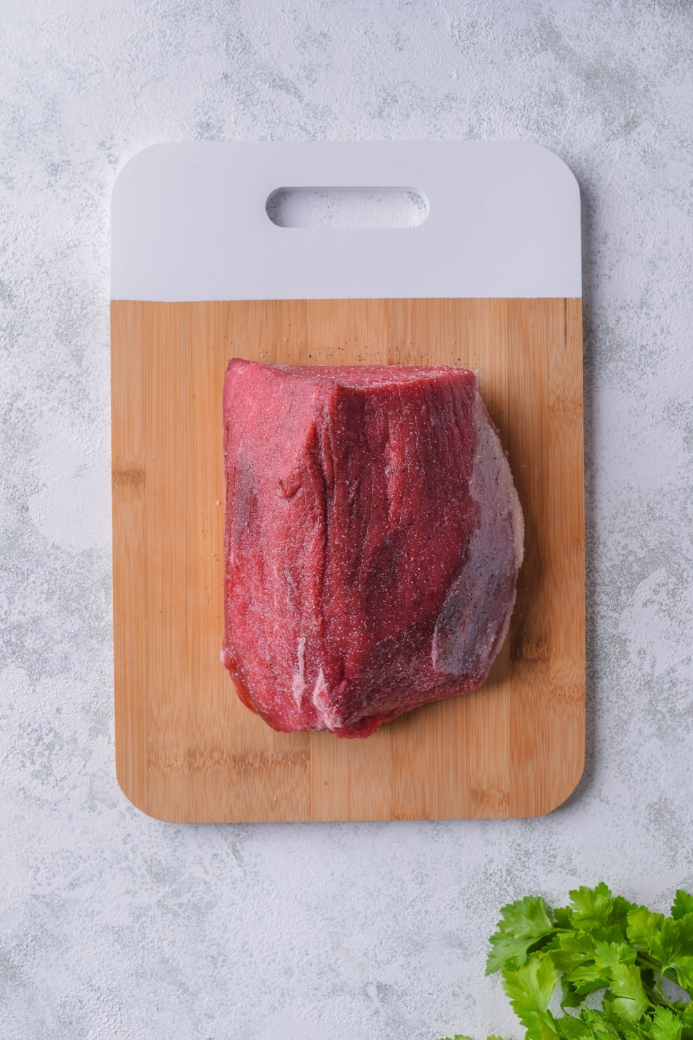 A raw eye of round steak on a wooden cutting board with a white handle.