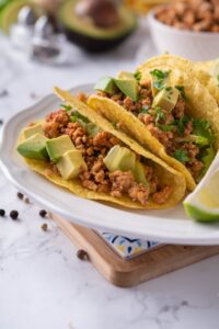 Close up of tacos stuffed with seasoned ground turkey, avocados, and cilantro on a plate with a lime wedge.