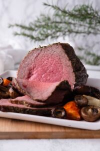 A medium rare sliced eye of round roast on a white rectangle plate with mushrooms and carrots