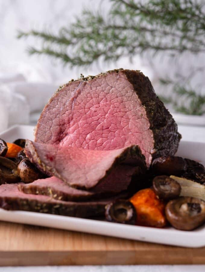 A medium rare sliced eye of round roast on a white rectangle plate with mushrooms and carrots