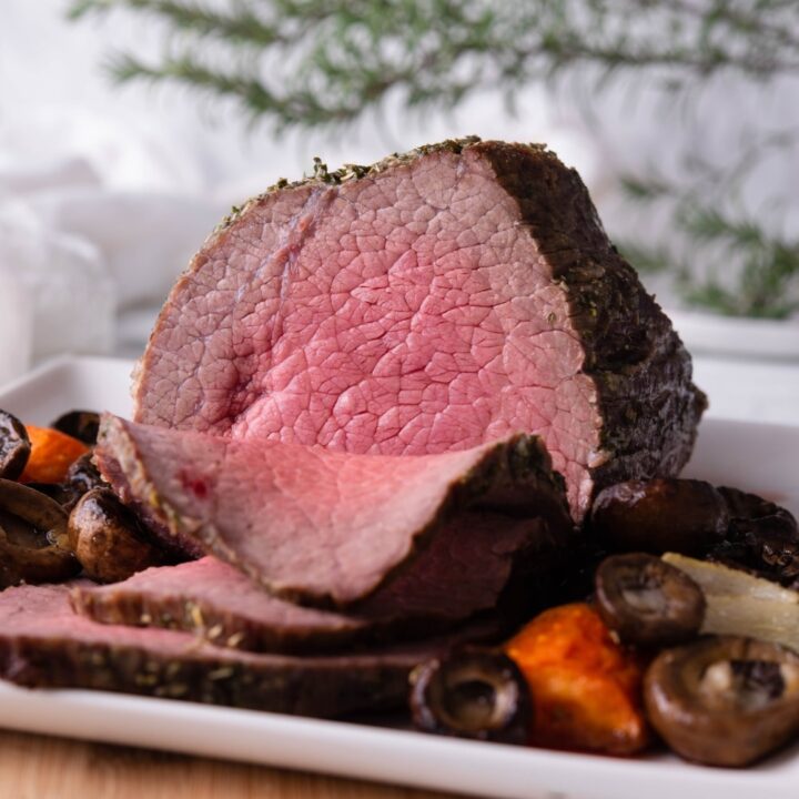 A medium rare sliced eye of round roast on a white rectangle plate with mushrooms and carrots