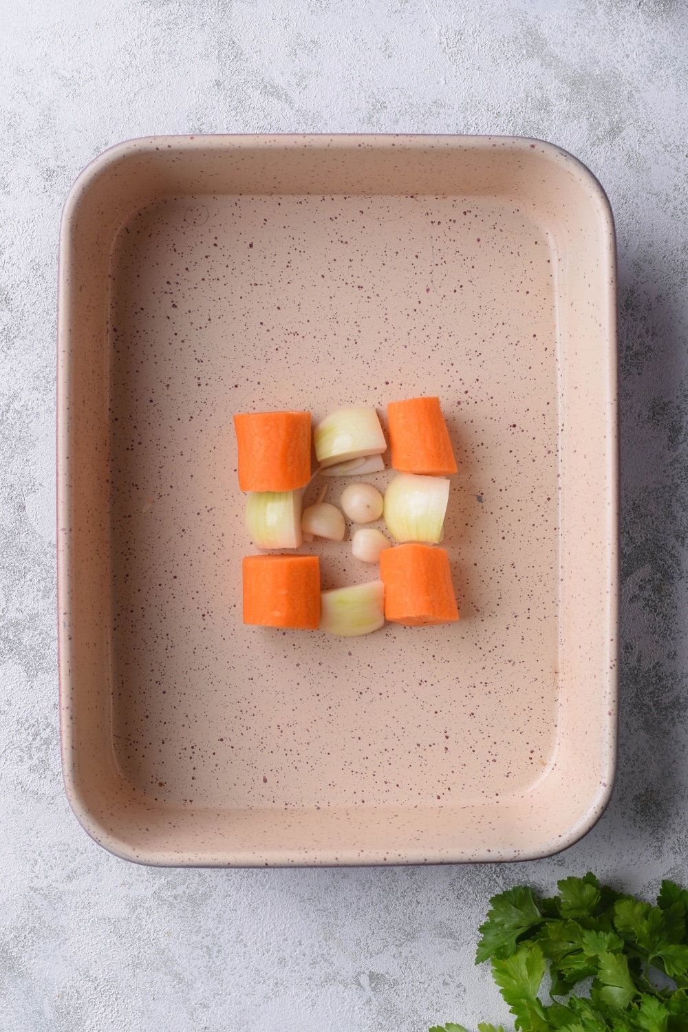 Chunks of carrots, onions, and garlic arranged in a small square in the center of a ceramic baking tray.