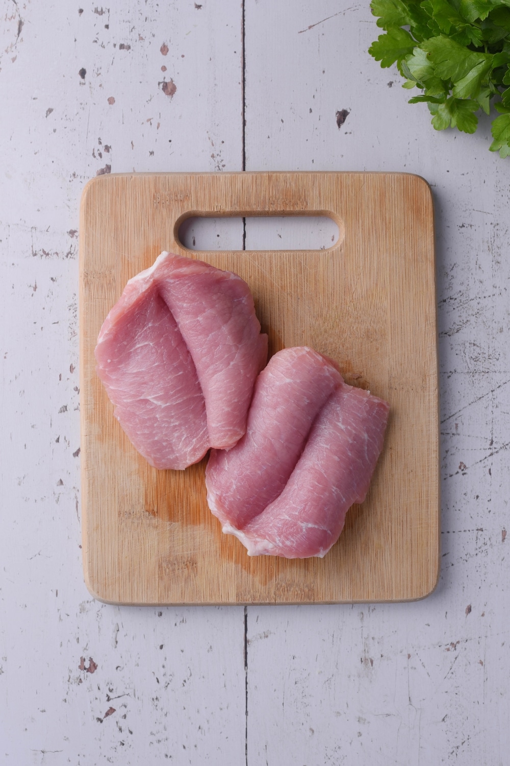Raw pork chops sliced down the middle and opened on a wooden cutting board.