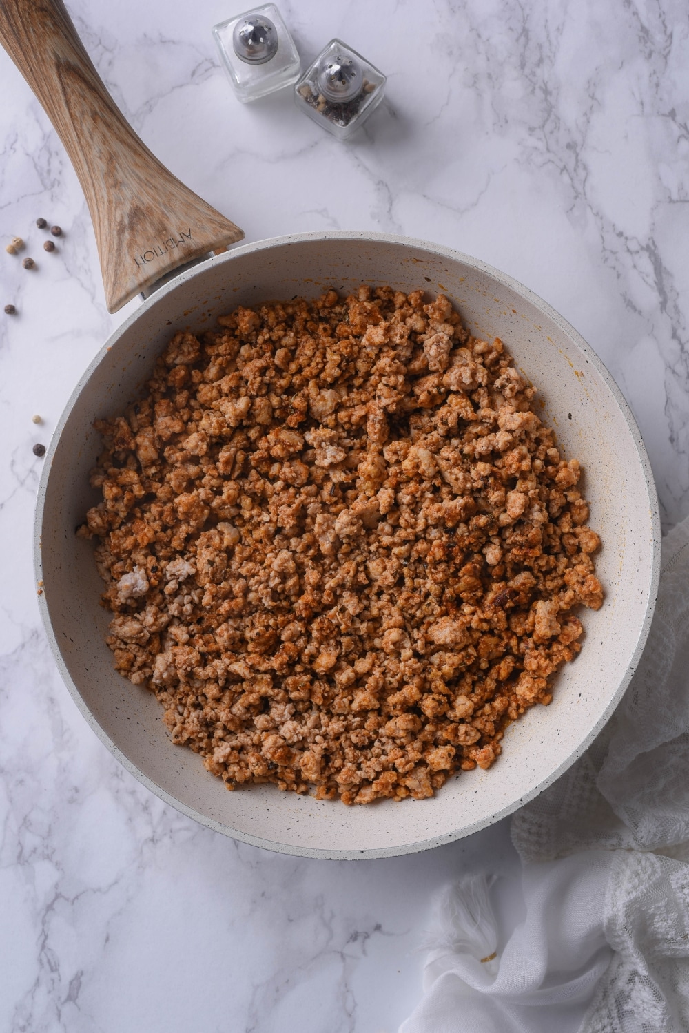 Seasoned cooked ground turkey in a white skillet with a wooden handle.