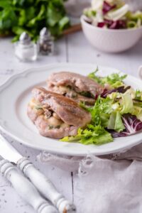 Pork chops stuffed with swiss cheese and mushrooms with fresh greens on a white plate.