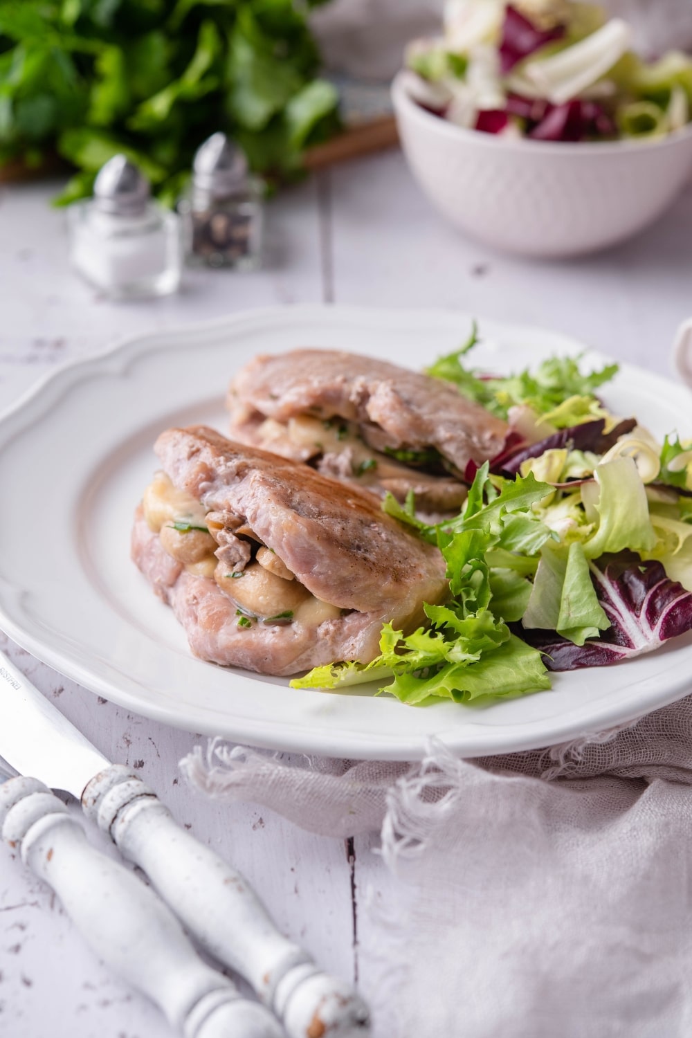 Pork chops stuffed with swiss cheese and mushrooms with fresh greens on a white plate.