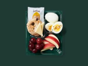 A Starbucks egg and cheddar protein box with apple slices, grapes, a peanut butter pack, cookie, cheese, and two hard boiled eggs.