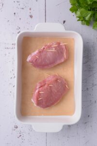 Stuffed pork chops closed with toothpicks on a ceramic baking dish.