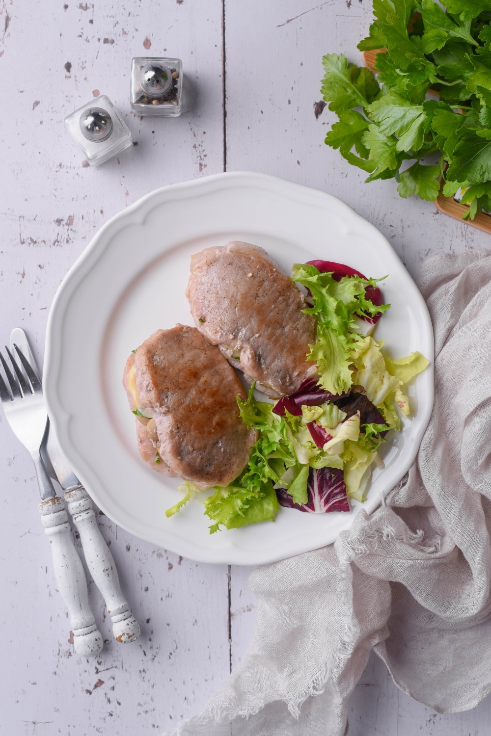 Top view of seared pork chops stuffed with swiss cheese and mushrooms with garden salad. The meal is on a white plate next a fork and knife.