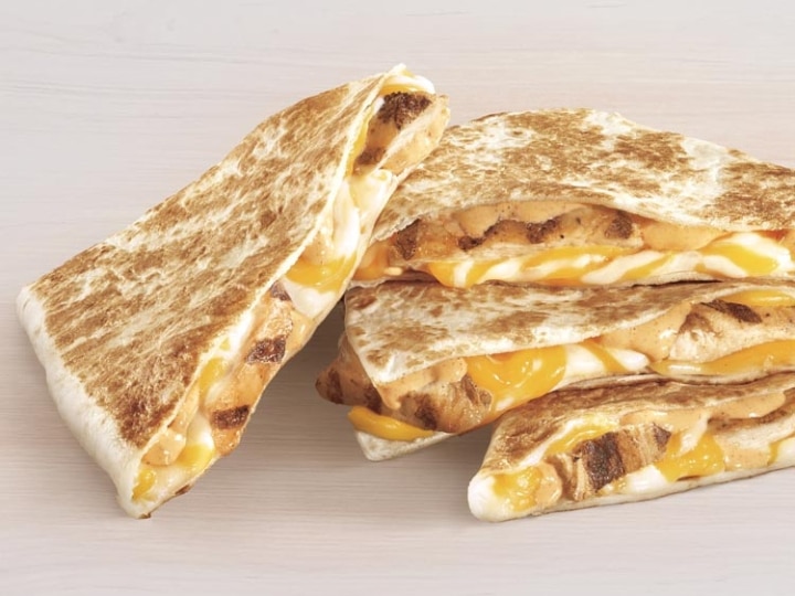 Four slices of Taco Bell cheese quesadilla. Three are stacked on top of one another and one is leaning against the stack.