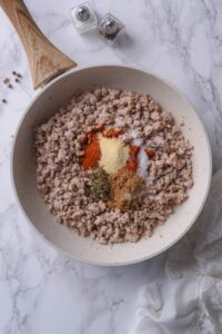 Cooked ground turkey topped with spices in a white skillet with a wooden handle.