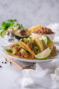 Crispy tacos stuffed with seasoned ground turkey, avocados, and cilantro on a plate with lime wedges.